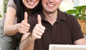 smilende ungt par giver thumbs up foran computer