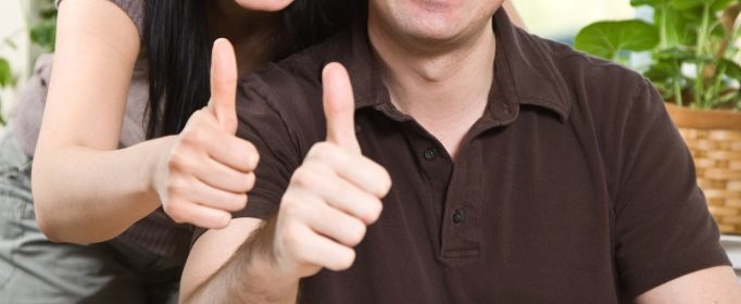 smilende ungt par giver thumbs up foran computer